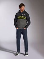 Alpinestars Parallel-hættetrøje, farveblokket pullover, sort og gunmetal-grå, skarpt gult Alpinestars-tekstlogo og hvidt stjernelogo på brystet, båret af en mandlig model med mørkeblå jeans og sorte sneakers, afslappet motorsport-streetwear