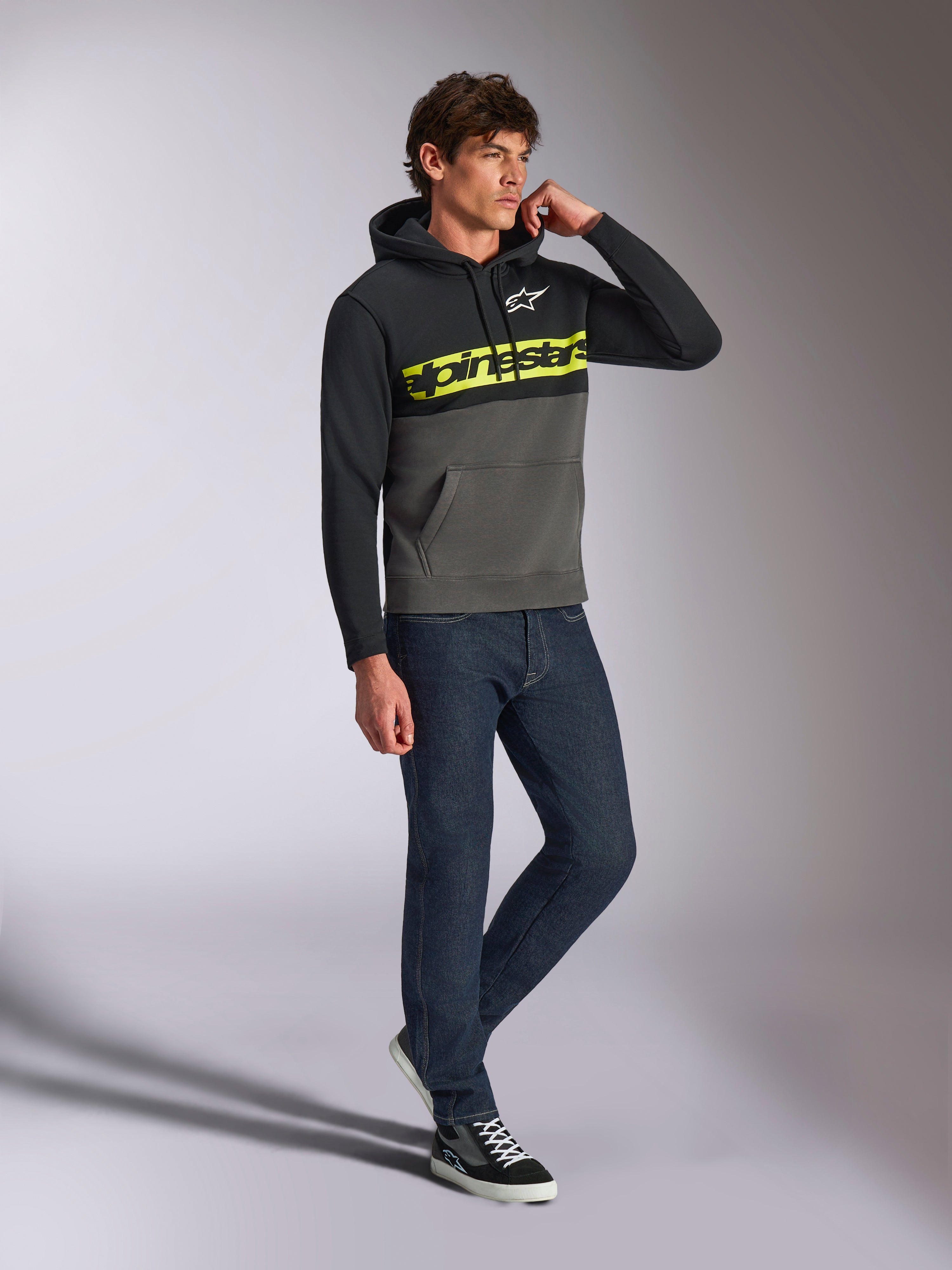 Alpinestars Parallel hættetrøje, afslappet streetwear, farveblokket sort og gunmetal grå, neongult Alpinestars-ordlogo på brystet, hvidt Astars-logo, hætte med snøre, båret med mørke jeans og sneakers