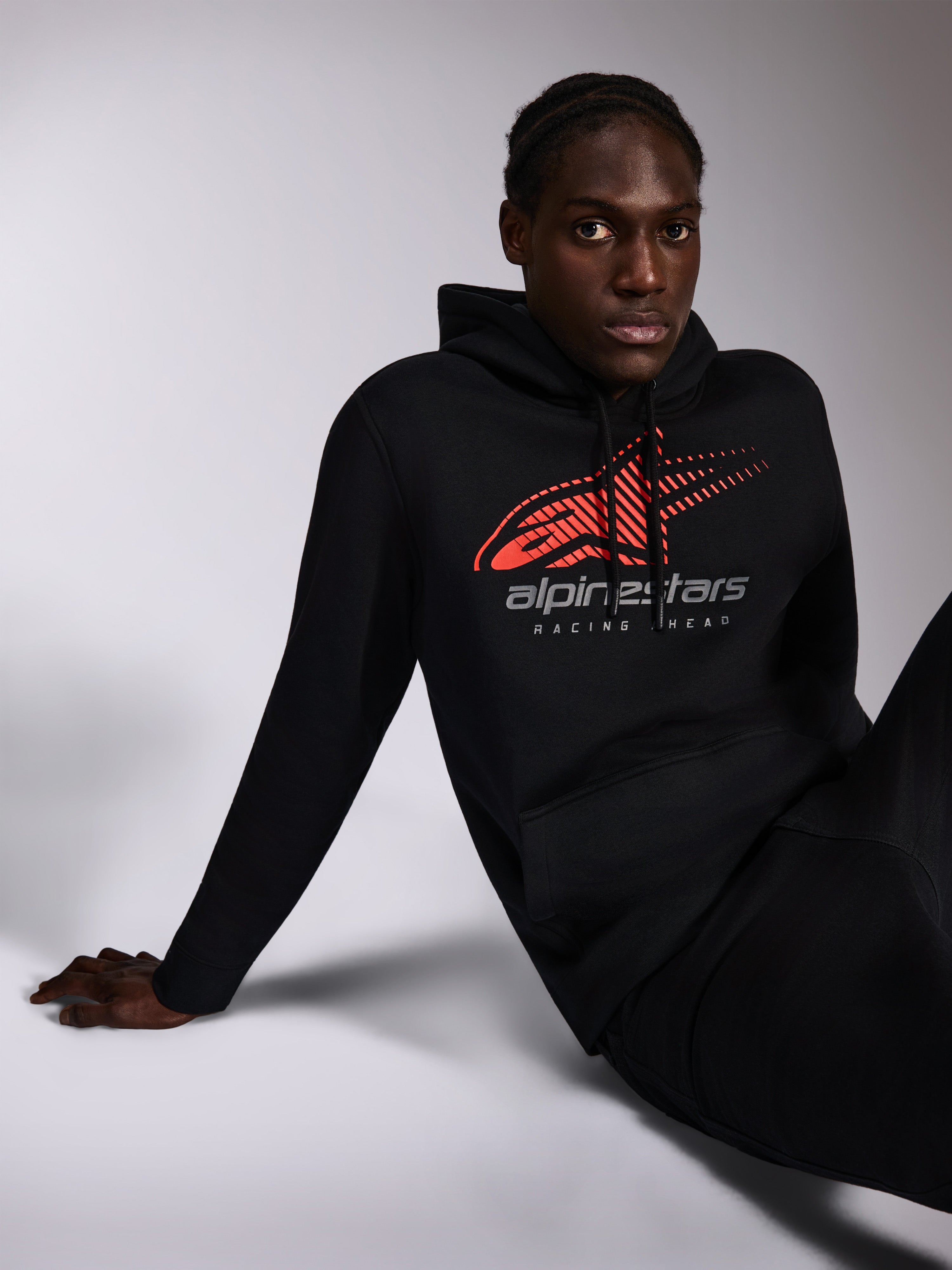 Alpinestars Pulse Hættetrøje, sort, afslappet streetwear båret af model, med rødt Astars-logo med speed line fade og 'alpinestars RACING AHEAD'-tekst på brystet, hætte med snoretræk, lange ærmer, moderne motorsport-inspireret design