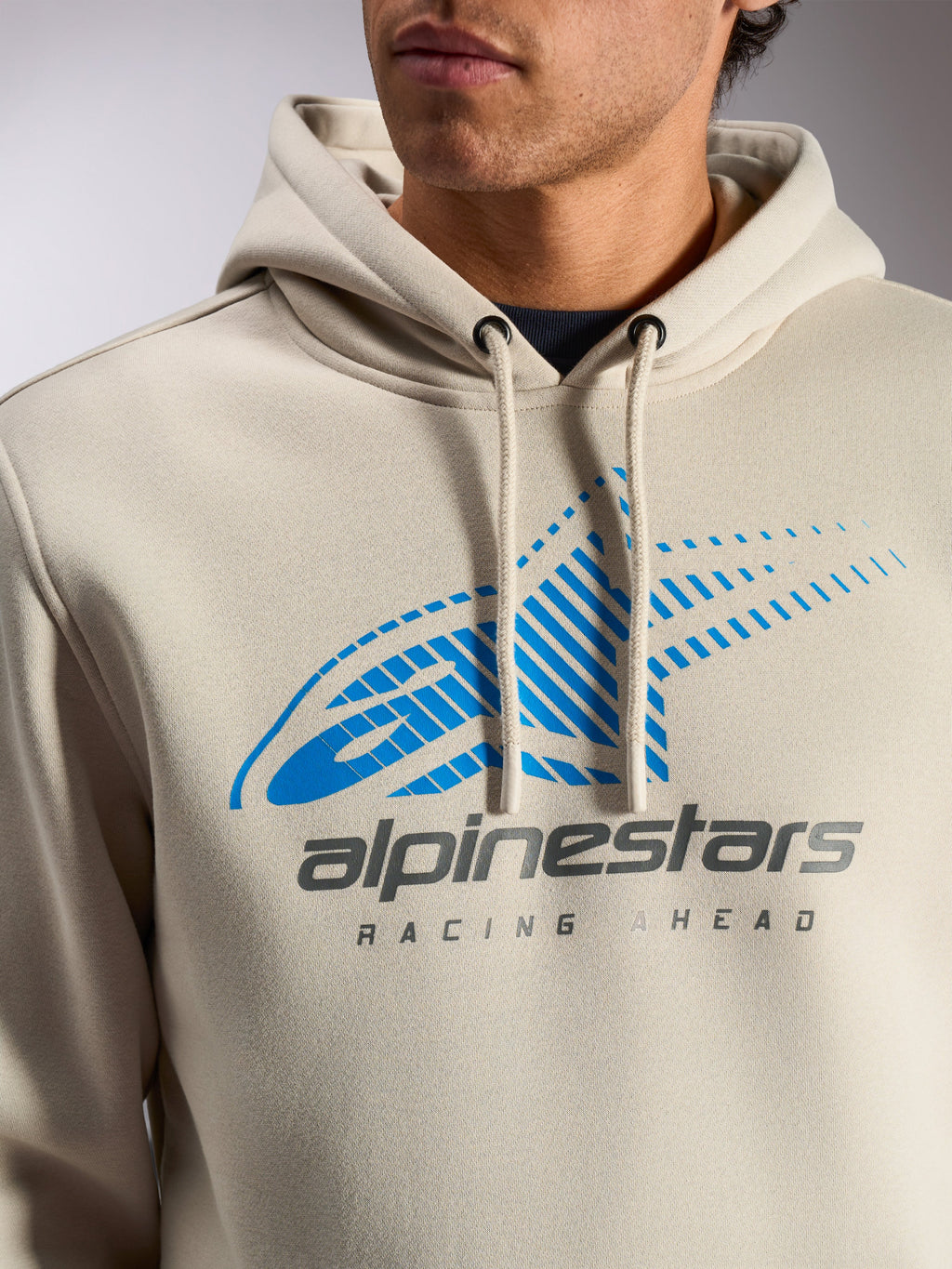 Alpinestars Pulse Hoodie, off-white afslappet streetwear pullover, tætbillede af brystet med blåt og gråt Astars Combo Logo med speed line fade og 'Racing Ahead'-tekst, hætte med snøre og dyppede snoreender.