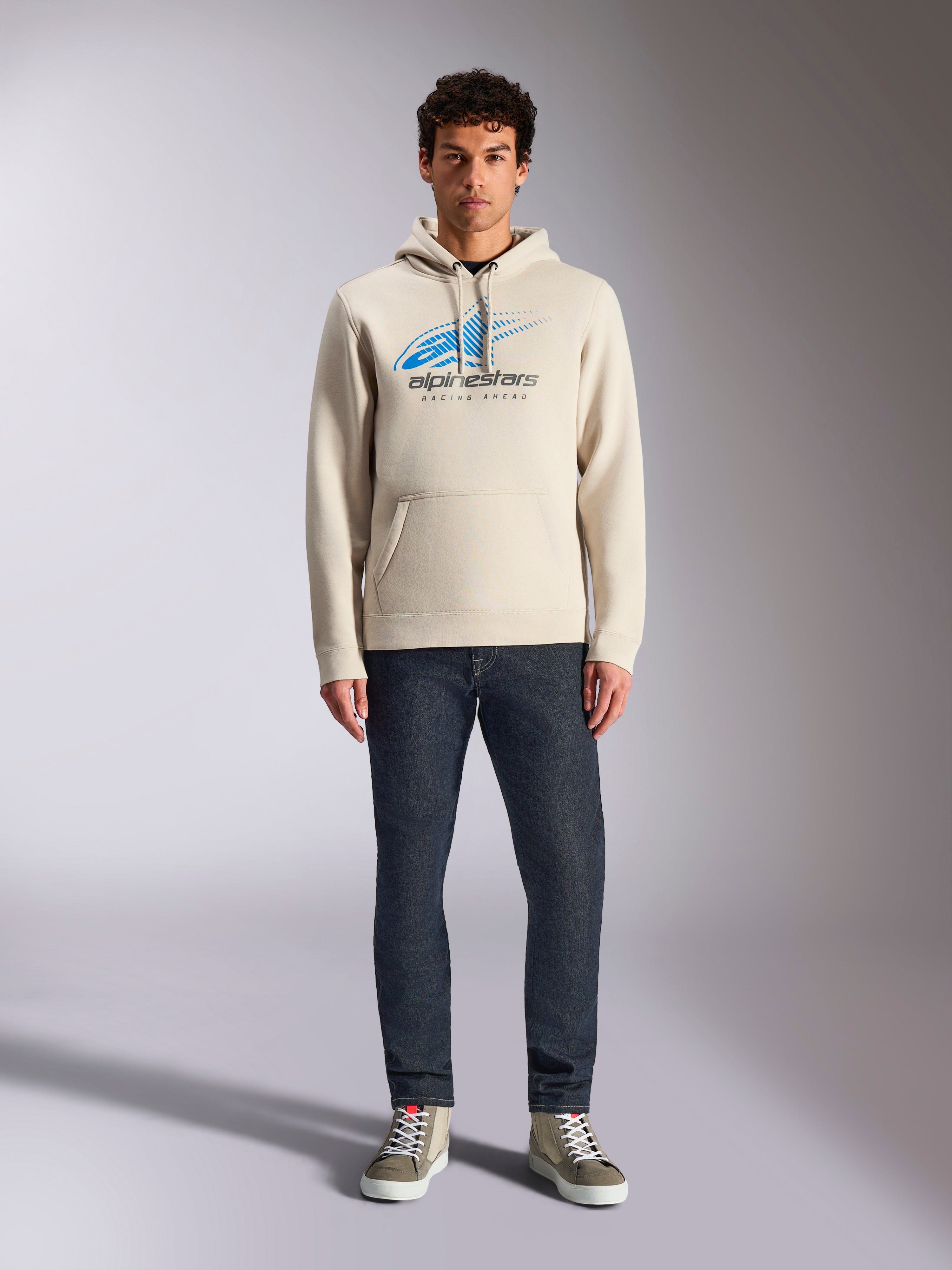 Alpinestars Pulse Hættetrøje, Off White, langærmet pullover med hætte og snøre, blå og sort Astars Combo Logo med speed line fade, stylet med mørke jeans og sneakers, afslappet motorsport-streetwear