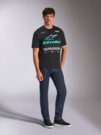 Alpinestars Aplomb Oversized CSF Tee, kortærmet T-shirt, sort, stort blågrønt og hvidt Alpinestars-logo med farveovergang, "Racing Ahead"-tekst og ternet mønster, kombineret med mørkeblå jeans og sorte sneakers, afslappet motorsport-streetwear