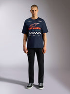 Alpinestars Aplomb Oversized CSF Tee, Short Sleeve Navy Blue T-Shirt, Large Chest Graphic with Orange and Red Gradient Logo and Checkered Pattern, worn by model with black pants and sneakers, Casual Motorsport Streetwear