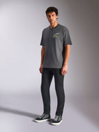 Alpinestars Overhang Oversized CSF Tee, kortærmet T-shirt, koksgrå, med hvidt Astars-logo og grøn tekst på brystet, båret af model med sorte bukser og sneakers, afslappet oversized pasform, casual motorsport-streetwear