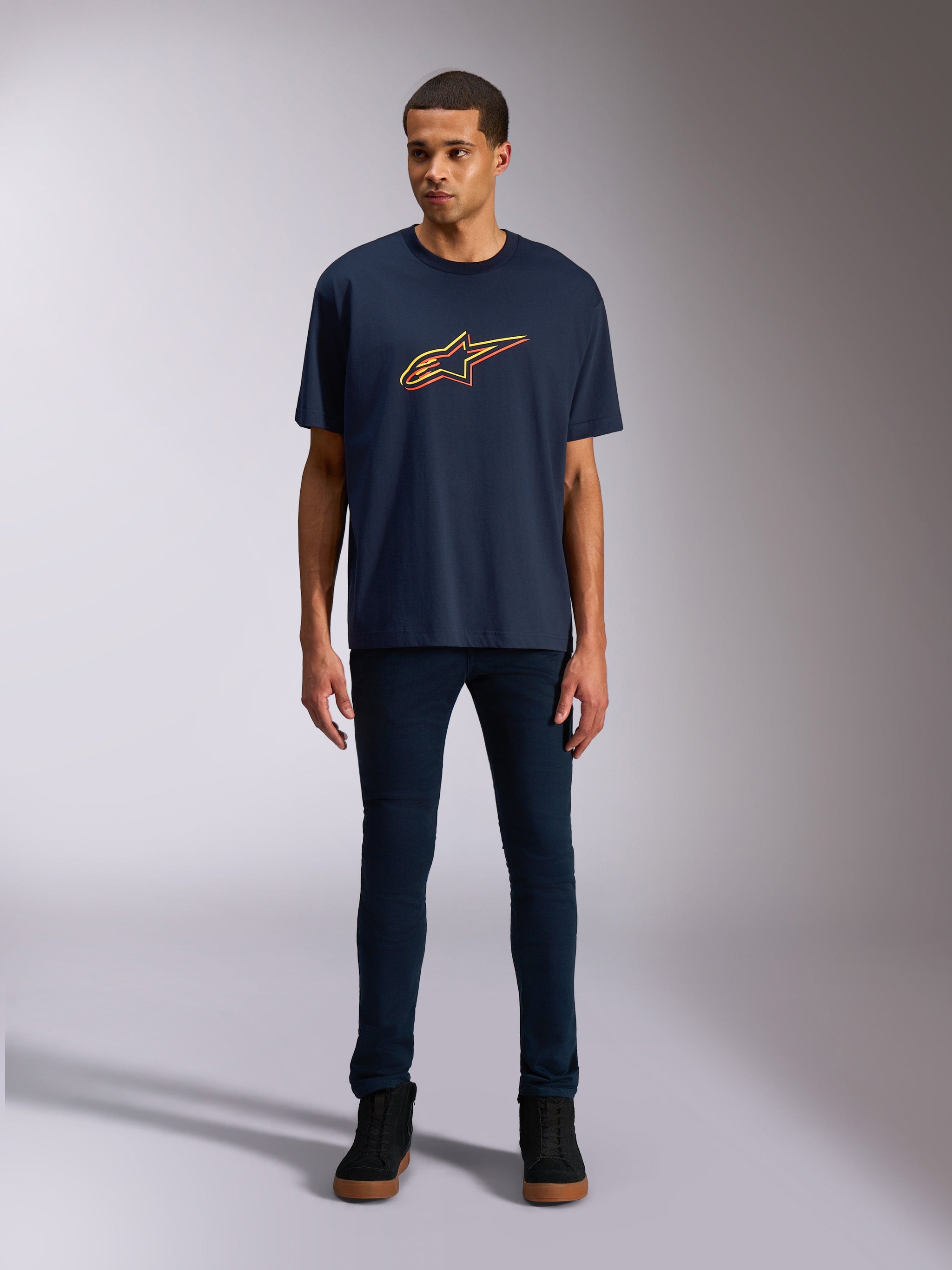 Alpinestars Alter Oversized CSF Tee, kortærmet T-shirt, marineblå, med Alpinestars stjerne-logo på fronten i gul og orange farveforskydning, båret af en model med mørke denimjeans og sorte sneakers, afslappet lifestyle-sportstøj