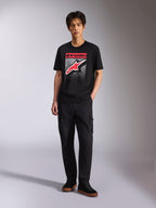 Alpinestars Noka CSF Tee, kortærmet t-shirt, sort, Astars-logo på fronten med rød og hvid MX-gradueringsgrafik, båret af en model med sorte cargobukser, afslappet motorsport-streetwear