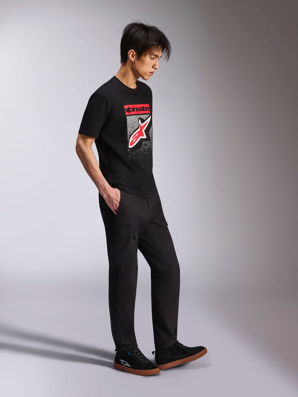Alpinestars Noka CSF Tee, kortærmet t-shirt, sort, Astars-logo på fronten med rød og hvid MX-graduering, båret med sorte cargobukser og sneakers, afslappet motorsport-inspireret streetwear