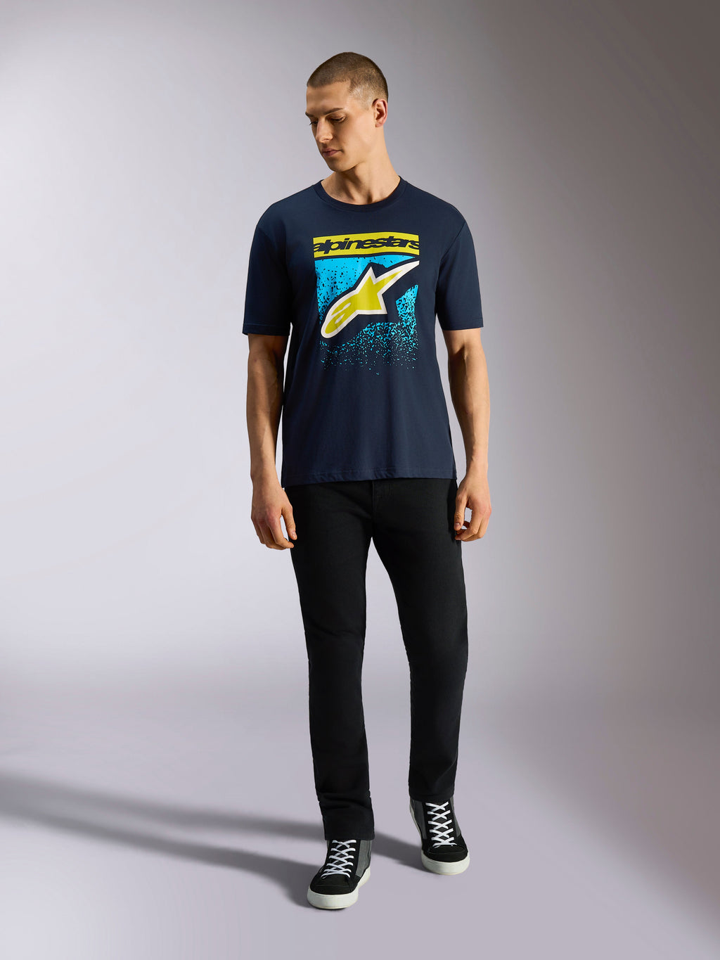 Alpinestars Noka CSF Tee, kortærmet t-shirt, mørkeblå, Astars-logo på fronten med gul og lyseblå MX-graduering, båret af en model med sorte bukser, casual motorsport streetwear