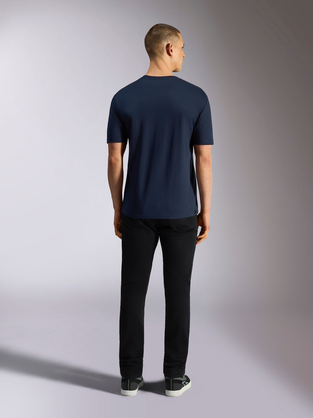 Alpinestars Noka CSF Tee, kortærmet t-shirt, marineblå, set bagfra af en mand iført t-shirten kombineret med sorte bukser og sneakers, afslappet motorsport streetwear