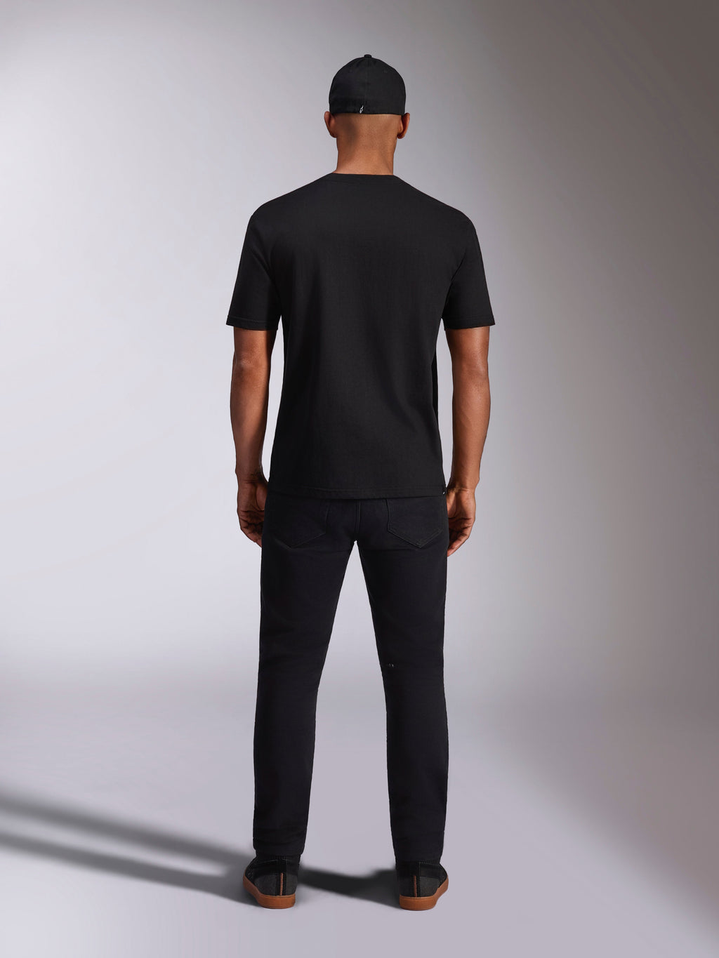 Alpinestars Ellipsoid CSF Tee, kortærmet T-shirt, sort, set bagfra på model med sort kasket og bukser, afslappet motorsport-inspireret streetwear
