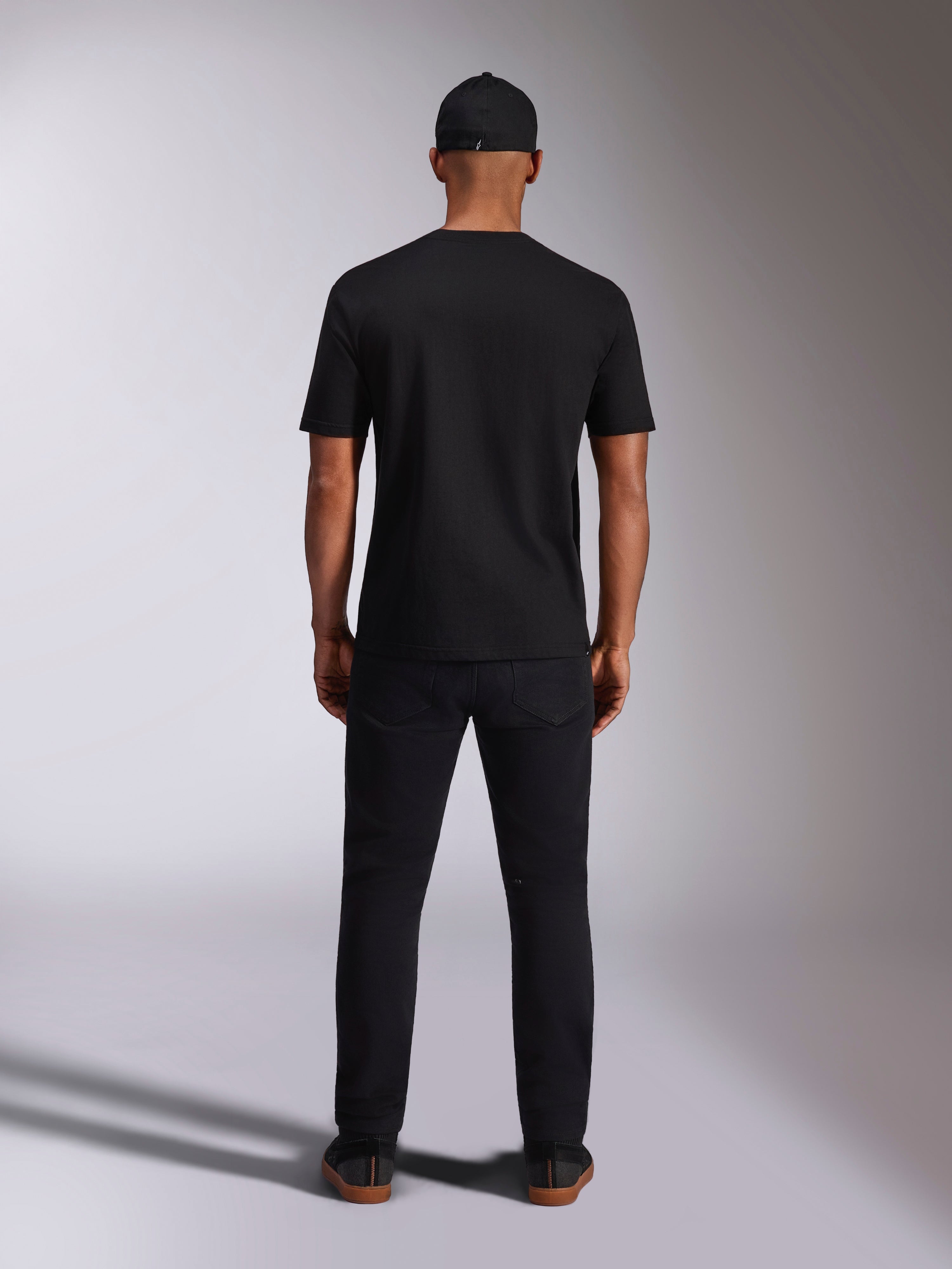 Alpinestars Ellipsoid CSF Tee, kortærmet T-shirt, sort, set bagfra på model med sort kasket og bukser, afslappet motorsport-inspireret streetwear