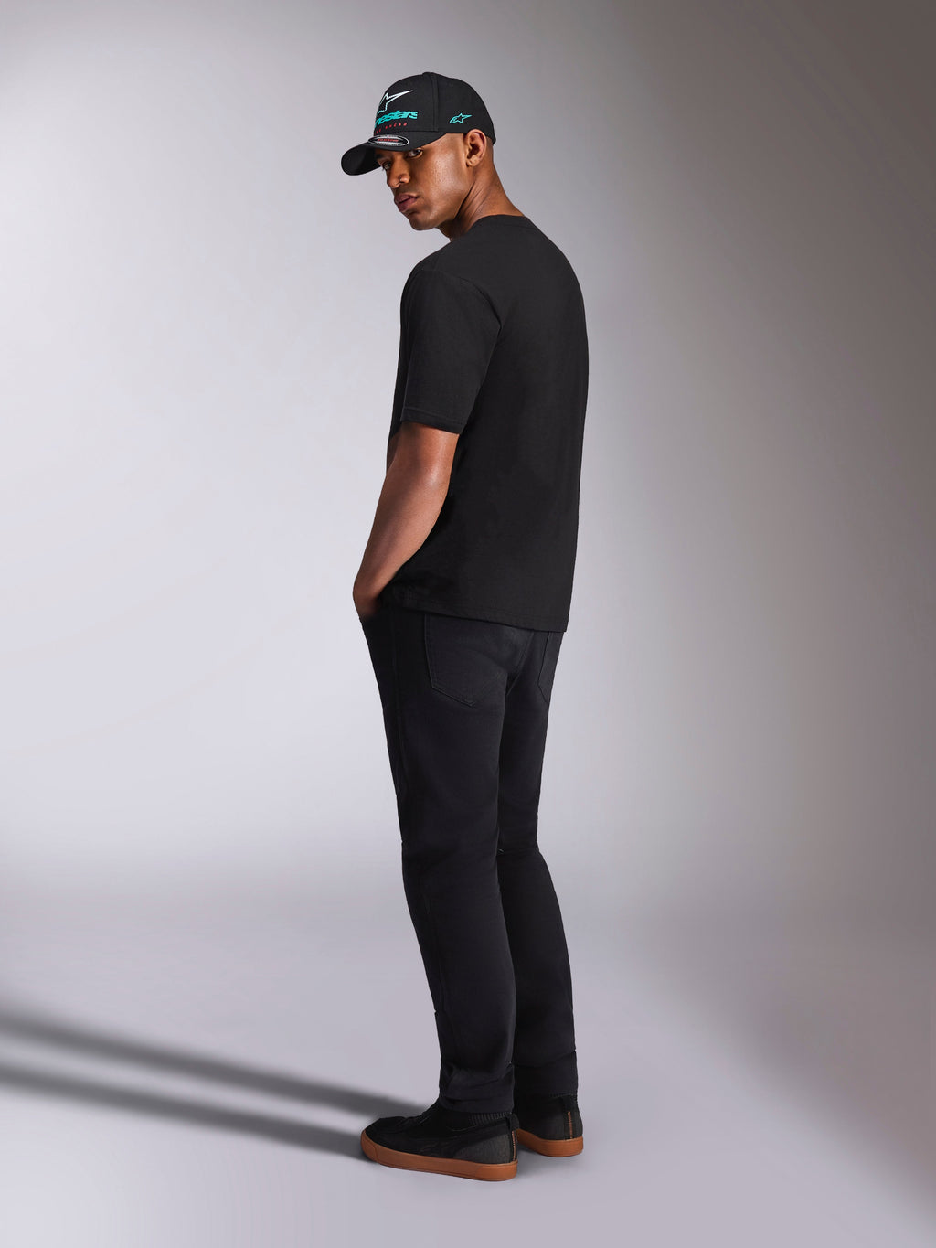 Alpinestars Ellipsoid CSF Tee, kortærmet T-shirt, sort, set bagfra på model iført sorte bukser og en sort Alpinestars kasket, afslappet motorsport-livsstilsoutfit