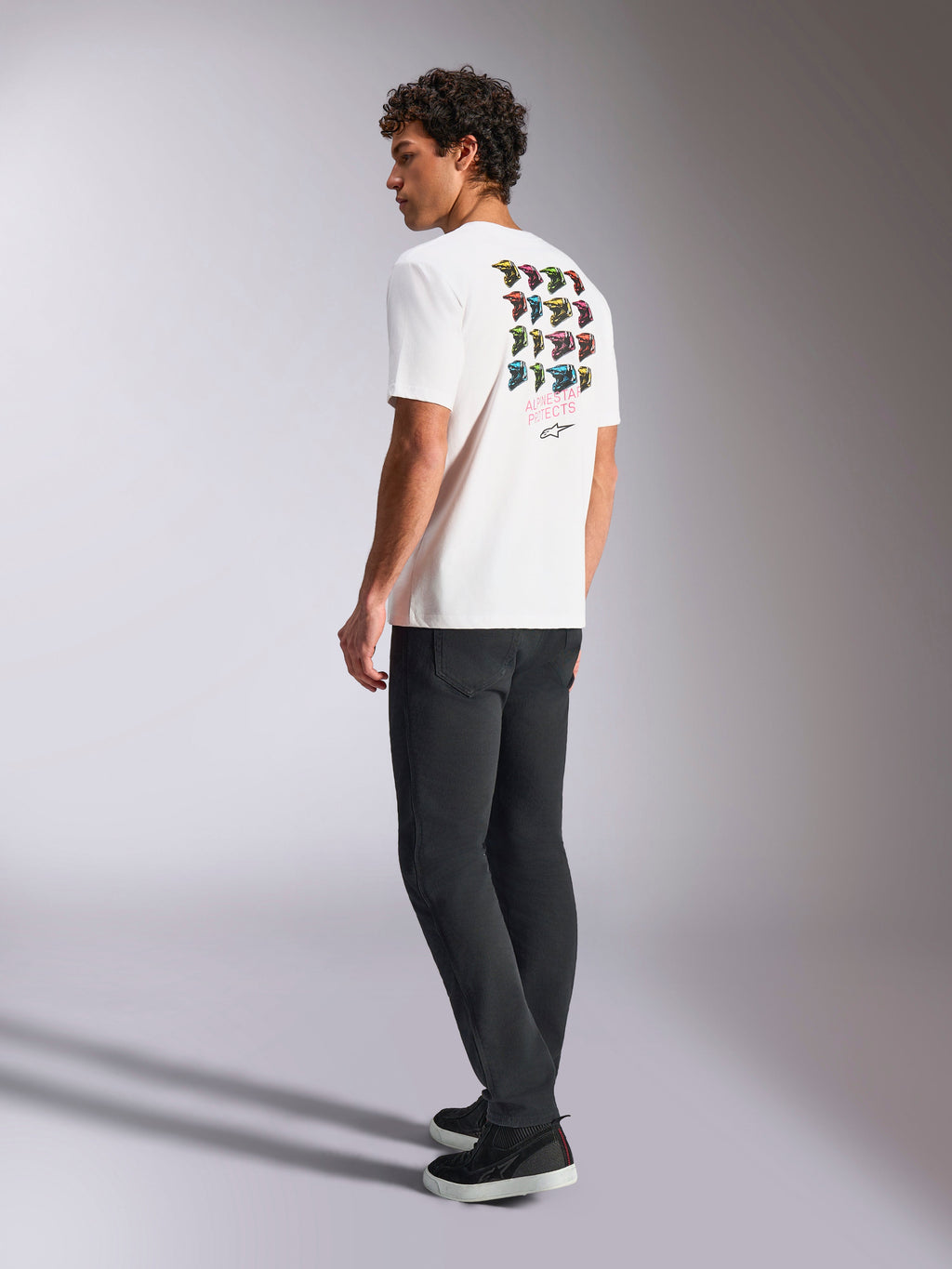 Alpinestars Pop Helmet CSF Tee, kortærmet T-shirt, hvid, set bagfra på model med farverig M10 hjelm-grafik, kombineret med mørke bukser og sorte sneakers, afslappet motorsport-inspireret streetwear