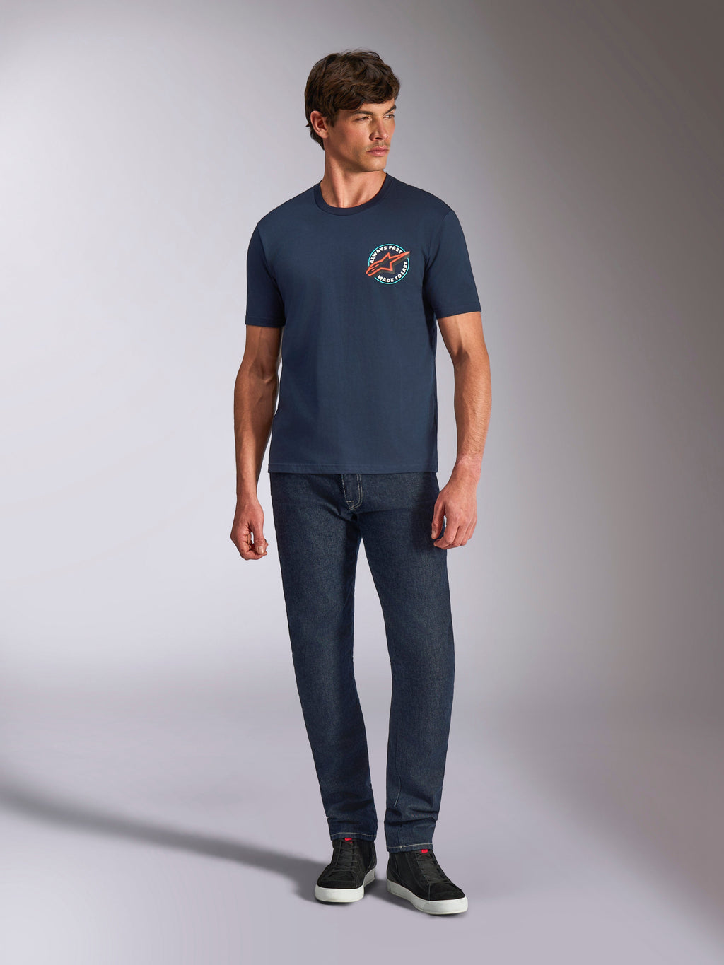 Alpinestars Aorbit CSF Tee, kortærmet T-shirt, navy, cirkulær brystgrafik med Always Fast Made to Last-tekst, kombineret med mørke jeans og sneakers, afslappet motorsport-lifestyle-tøj