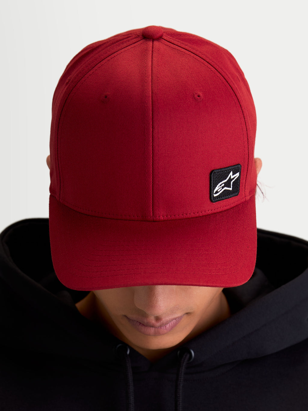 Alpinestars Pivot kasket, mørkerød baseball-kasket i sportswear-stil, unisex, med buet skygge, struktureret krone og et lille sort broderet Astars-logo patch på slidstærkt twill-materiale, vist på model.