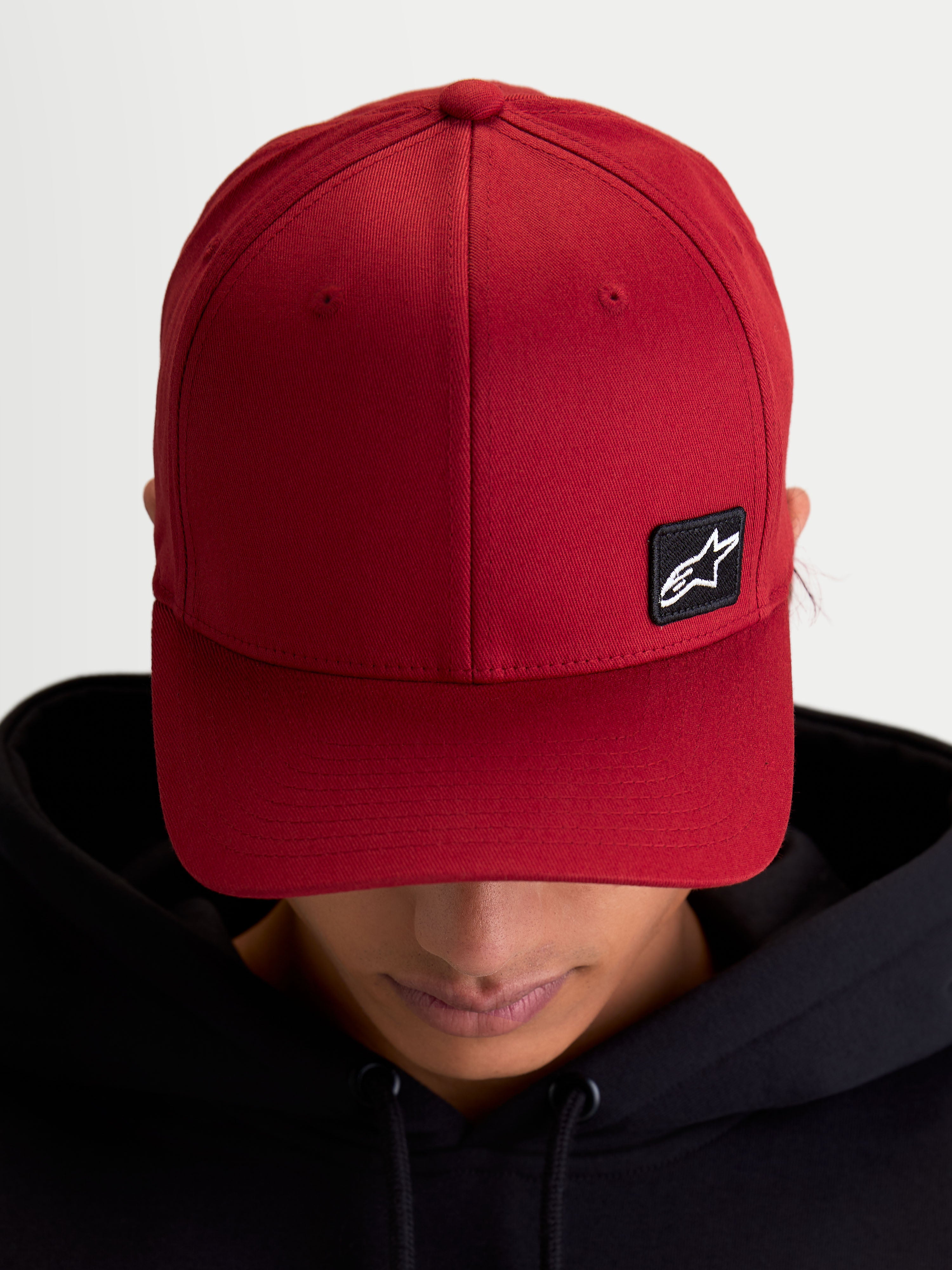 Alpinestars Pivot kasket, mørkerød baseball-kasket i sportswear-stil, unisex, med buet skygge, struktureret krone og et lille sort broderet Astars-logo patch på slidstærkt twill-materiale, vist på model.