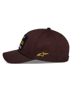 Alpinestars Matrix Snapback kasket, brun, set fra siden, buet skygge med sort snordetalje, broderet mærke på fronten, gult Astars-logo på siden, struktureret bomuldstwill-konstruktion, afslappet motorsport-hovedbeklædning