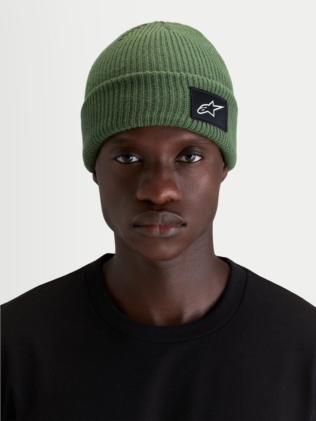 Alpinestars Unload Rib Cuff Beanie, sportswear knit winter hat, green, worn by a model showcasing the shallow-fit silhouette and SAstars woven front patch