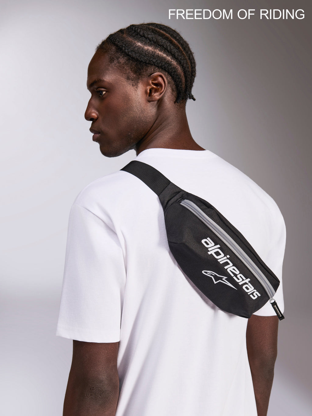 Alpinestars Only Linear hoftebæltetaske, sort og hvid crossbody-bæltetaske til sportstøj, 2L kapacitet, slidstærk 600D polyester, vist på en model over en hvid t-shirt til hverdagsbrug og urban pendling.