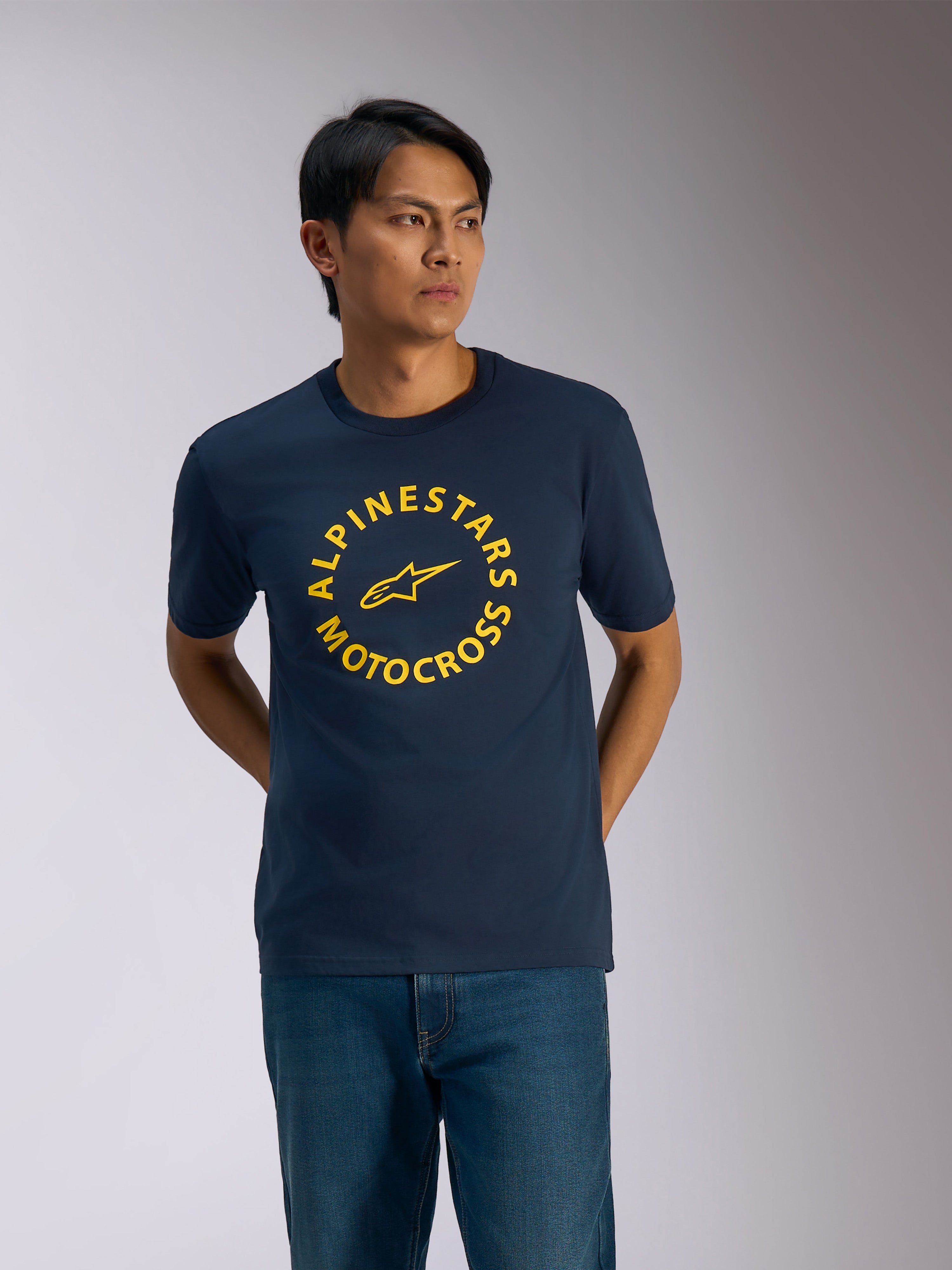Alpinestars MX CSF Tee, kortærmet t-shirt, navyblå, gul cirkulær Alpinestars Motocross-grafik med centralt stjernelogo, båret af en mand med blå jeans, afslappet motorsport-streetwear