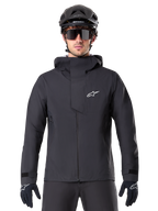 Alpinestars A-Dura Elite vandtæt jakke, sort, mountainbike-jakke, design med høj krave og hætte, lynlås foran med beskyttende brystklap og hvidt logo, vist med sort hjelm og cykelhandsker, teknisk vejrbeskyttelse til trail-kørsel