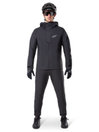 Alpinestars A-Dura Elite vandtæt jakke, sort, båret med matchende cykelbukser og handsker, sort hjelm og solbriller, med et hvidt Astars-logo på brystet, højtydende teknisk design til mountainbiking