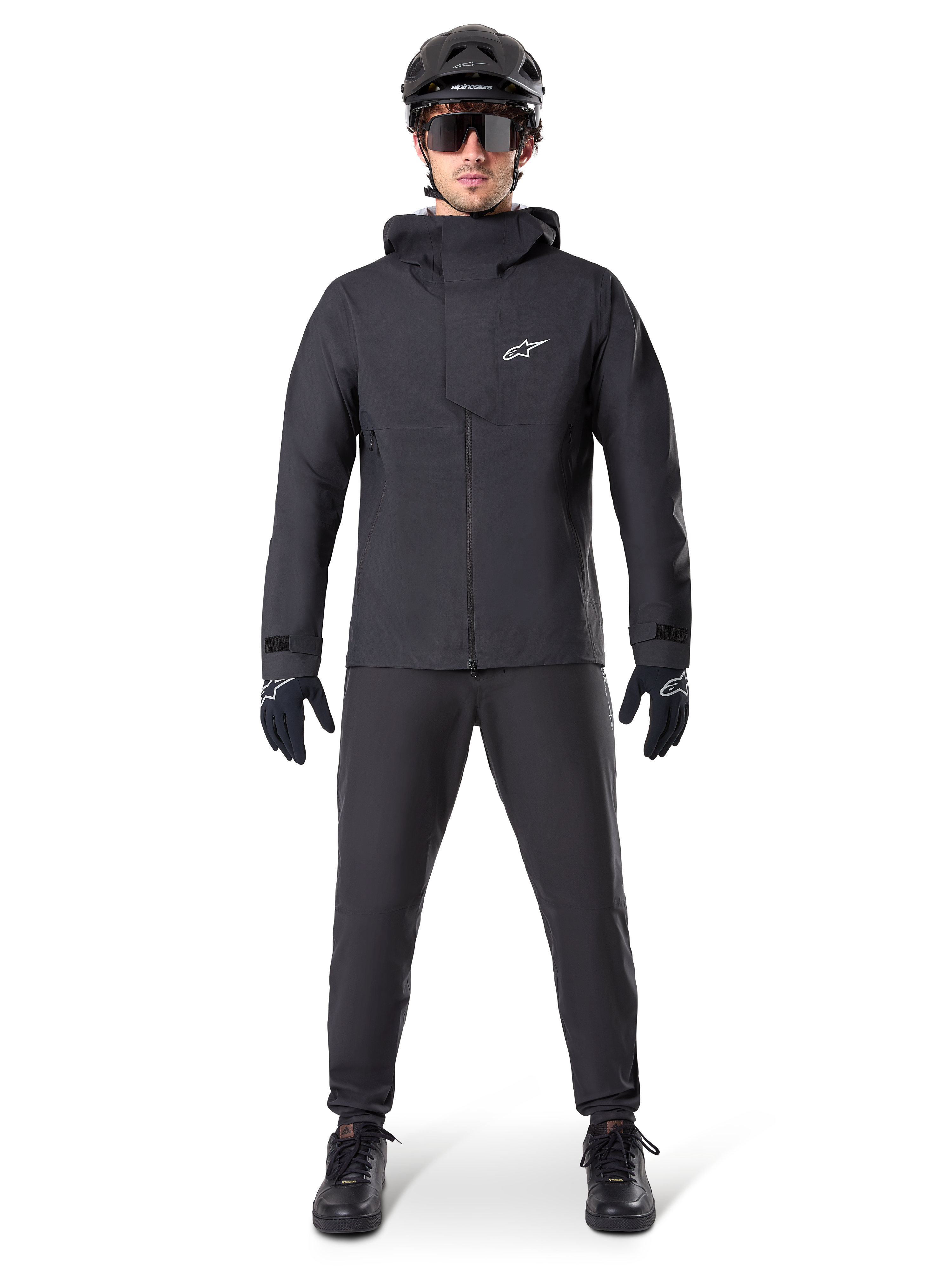 Alpinestars A-Dura Elite vandtæt jakke, sort, båret med matchende cykelbukser og handsker, sort hjelm og solbriller, med et hvidt Astars-logo på brystet, højtydende teknisk design til mountainbiking