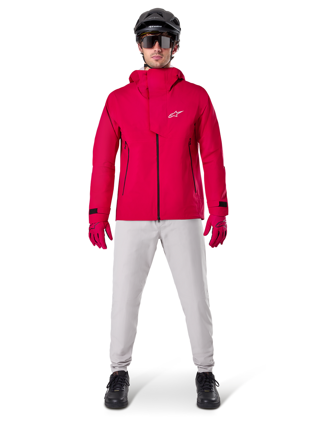 Alpinestars A-Dura Elite vandtæt jakke, Red Fluo, teknisk mountainbike-jakke båret med en sort MTB-hjelm, solbriller, matchende røde handsker og lysegrå bukser, fuldkropsvisning af cykeludstyr til alle vejrforhold