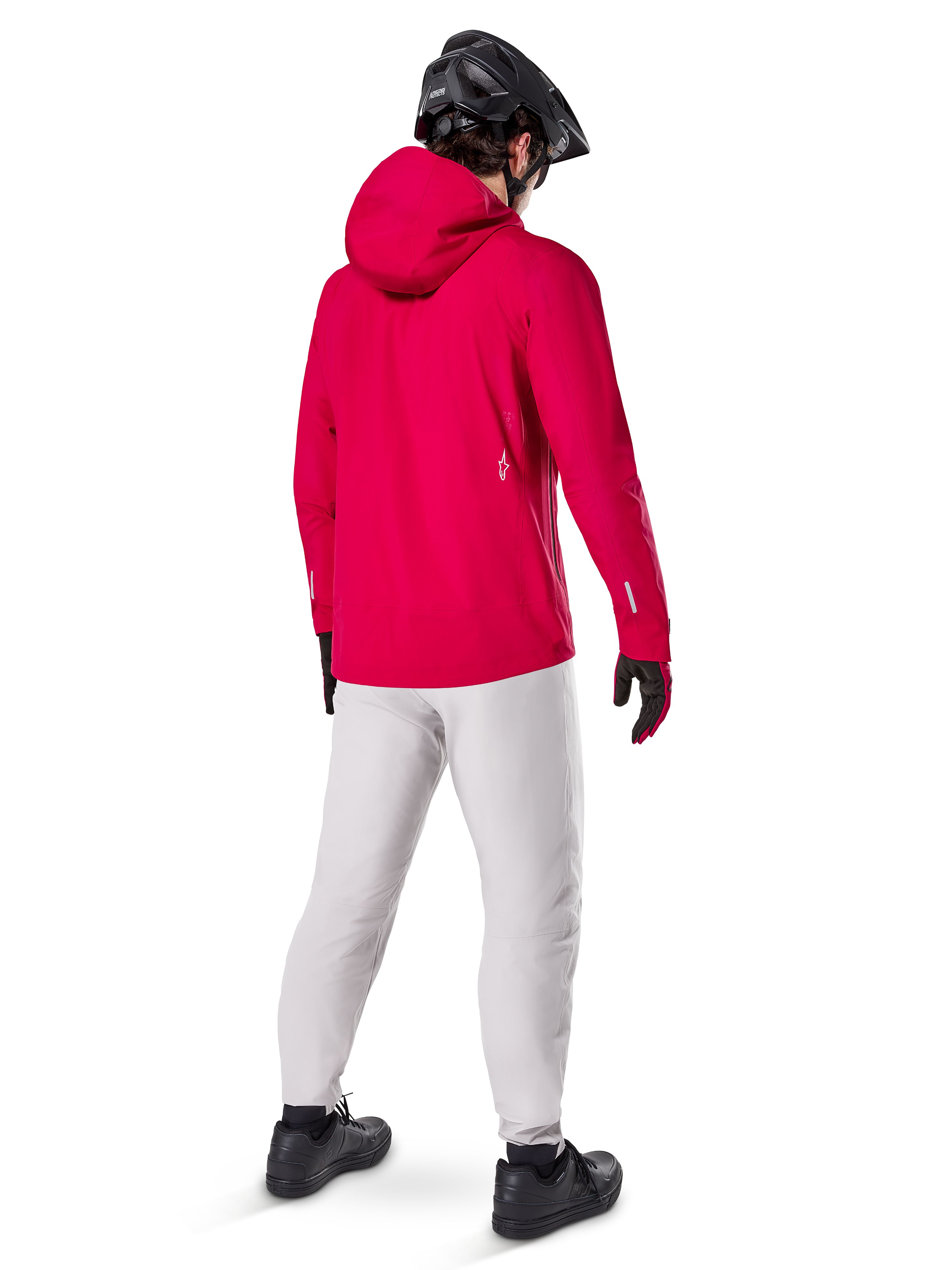 Alpinestars A-Dura Elite vandtæt jakke, Red Fluo, set bagfra i trekvart profil, båret med lysegrå bukser og sort MTB-hjelm, har hætte og reflekterende detaljer, højtydende cykelregnjakke til trail-kørsel