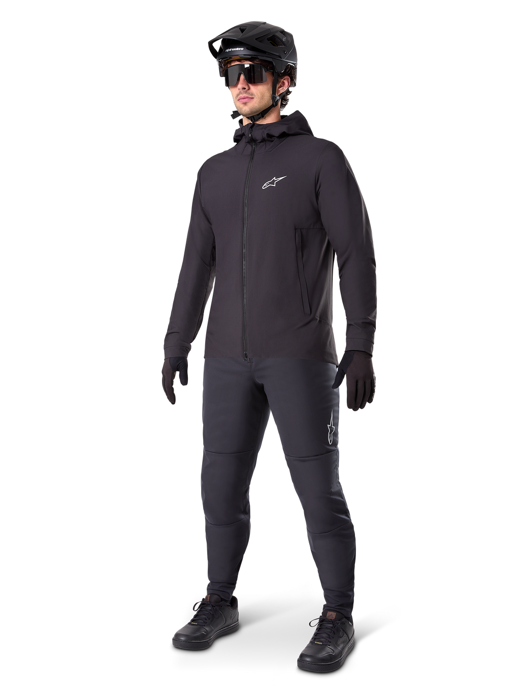 Alpinestars A-Dura Thermal jakke i sort, båret af en mandlig rytter med komplet mountainbike-udstyr inklusive sort hjelm, solbriller og cykelbukser, let isoleret jakke med hætte til cykelperformance i koldt vejr.
