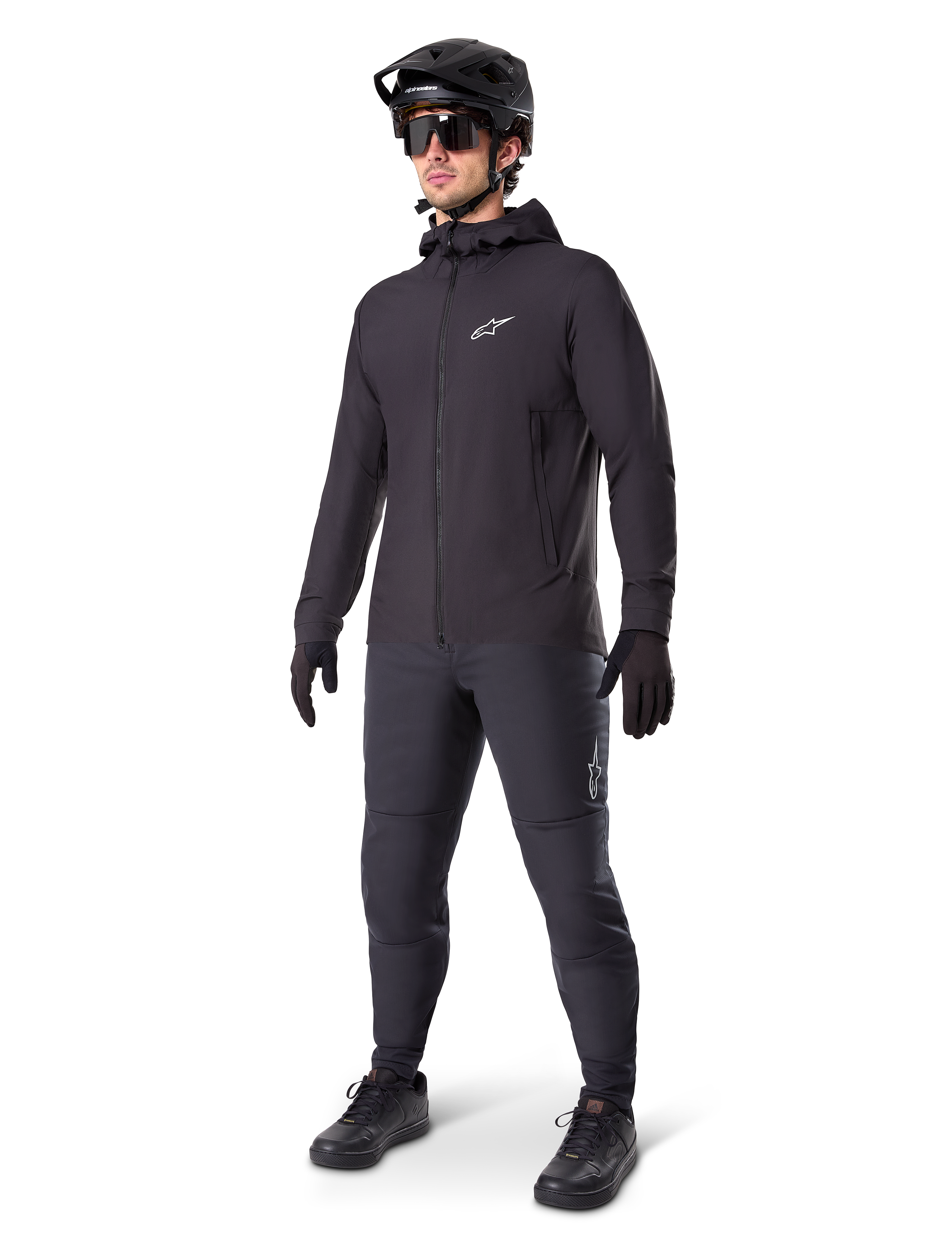 Alpinestars A-Dura Thermal jakke i sort, båret af en mandlig rytter med komplet mountainbike-udstyr inklusive sort hjelm, solbriller og cykelbukser, let isoleret jakke med hætte til cykelperformance i koldt vejr.