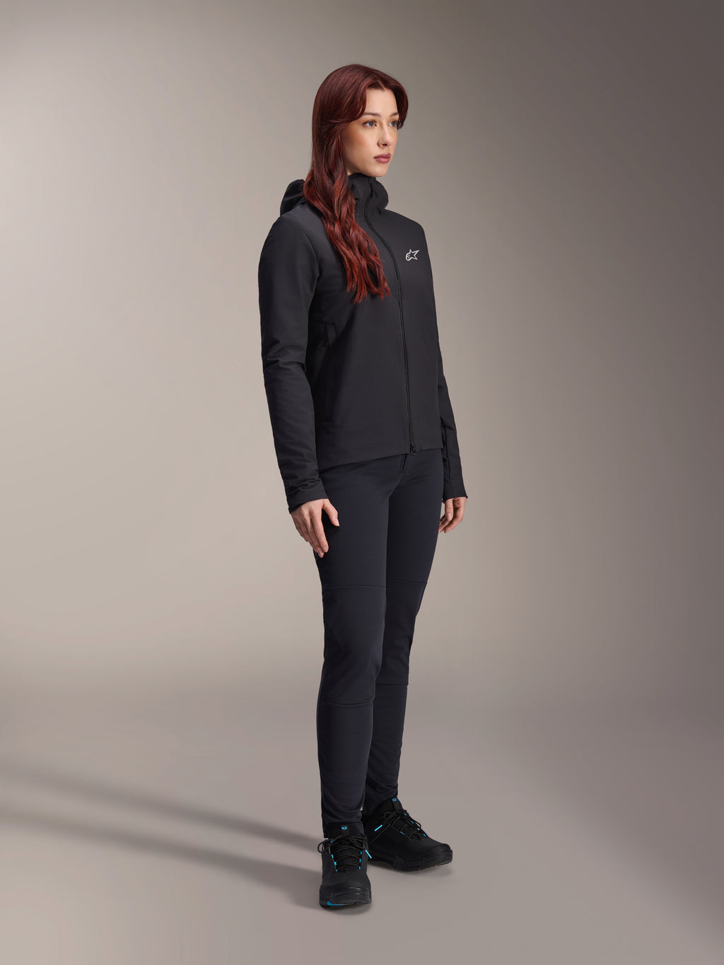 Alpinestars Stella A-Dura termojakke, let sort isoleret jakke til kvinder med hætte, kombineret med sorte bukser og sorte sko, professionelt cykel- og mountainbike-outfit til kolde vejrforhold