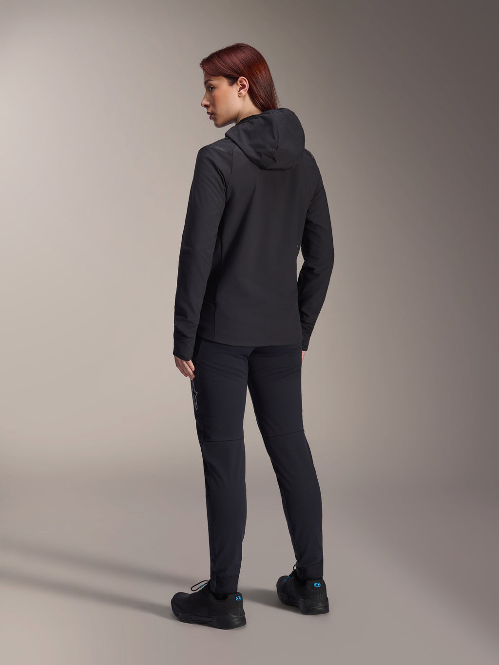 Alpinestars Stella A-Dura termojakke, MTB-cykeljakke til kvinder, sort, set bagfra med fokus på den isolerede hætte og regulær pasform, båret med matchende sorte bukser og sko, letvægts termisk isolering til kørsel i koldt vejr