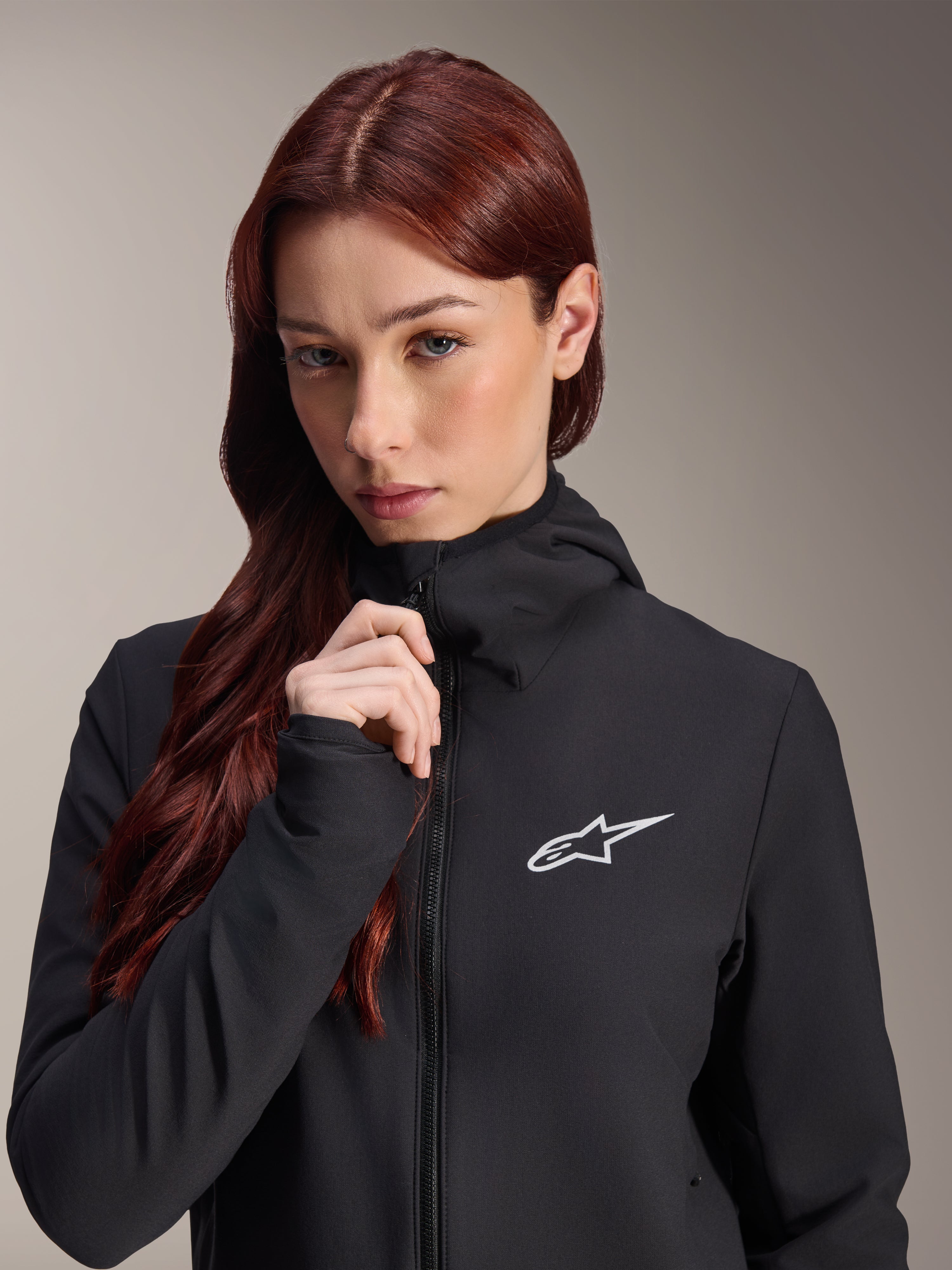 Alpinestars Stella A-Dura termojakke, sort cykeljakke til kvinder, båret af en model med langt rødbrunt hår, hvidt Alpinestars-logo på brystet, hættedesign med gennemgående lynlås, mountainbike-beklædning