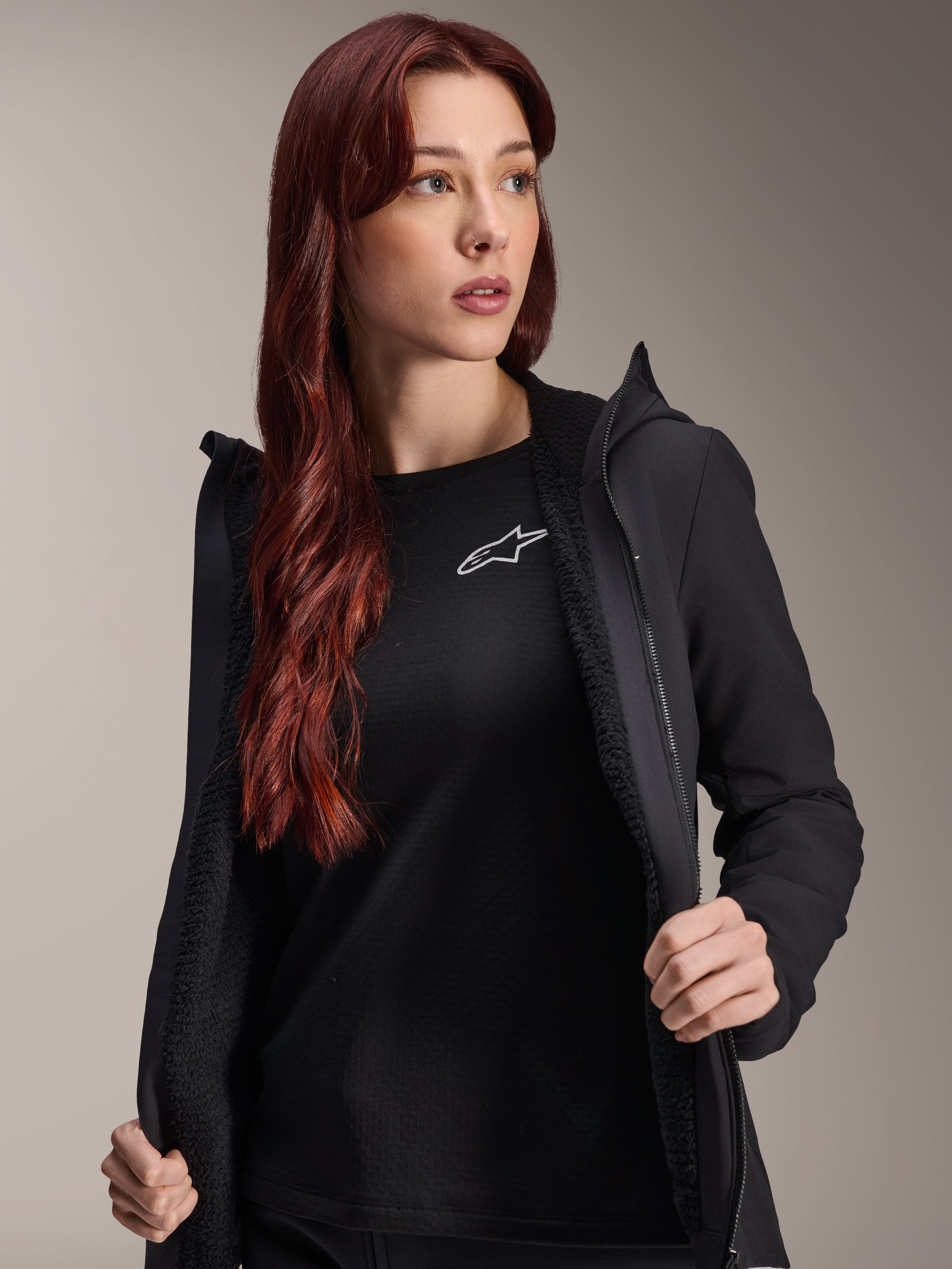 Alpinestars Stella A-Dura termojakke, sort cykeljakke til kvinder, vist åben med tekstureret fleecefor og lynlås foran, båret over en sort t-shirt med Alpinestars-logo, let og isoleret til cykling i koldt vejr