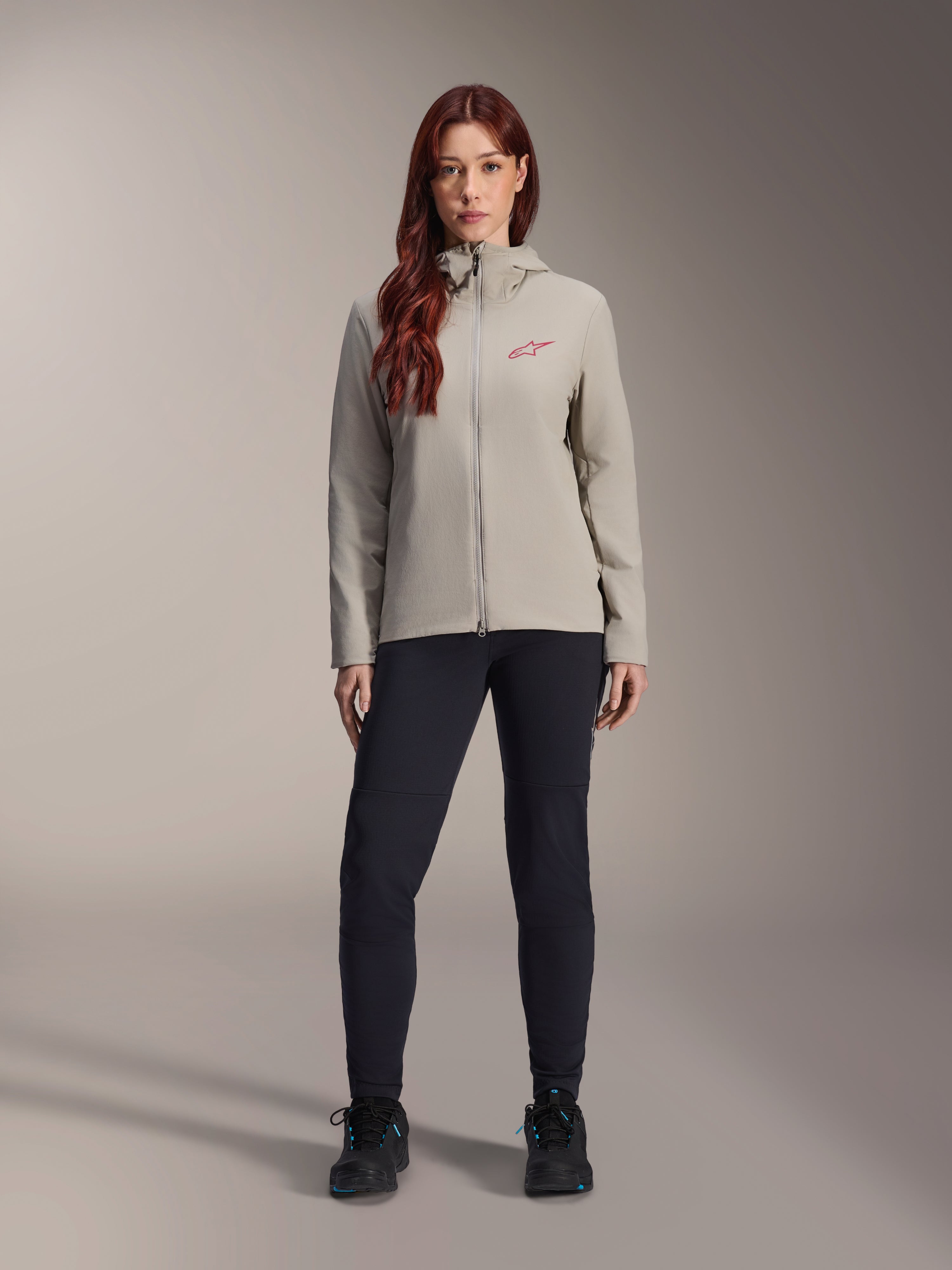 Alpinestars Stella A-Dura termojakke til kvinder, mountainbike-jakke, titaniumgrå, båret med sorte tekniske bukser og sort fodtøj, med fleece-foret hætte og rødt logo på brystet, designet til kørsel i koldt vejr