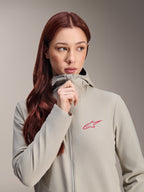 Alpinestars Stella A-Dura termojakke til kvinder, titaniumgrå med lyserødt Alpinestars-stjernelogo, model med langt rødt hår, der bærer og lyner den hætteklædte jakke, letvægtsisoleret cykeltøj til koldt vejr