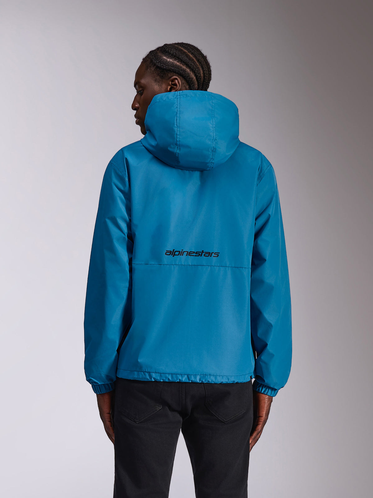 Alpinestars Speeder Chromium Windbreak Jakke, blå, set bagfra på model, viser sort ordlogo på ryggen, let vindjakke med hætte og elastiske manchetter, afslappet sportstøj