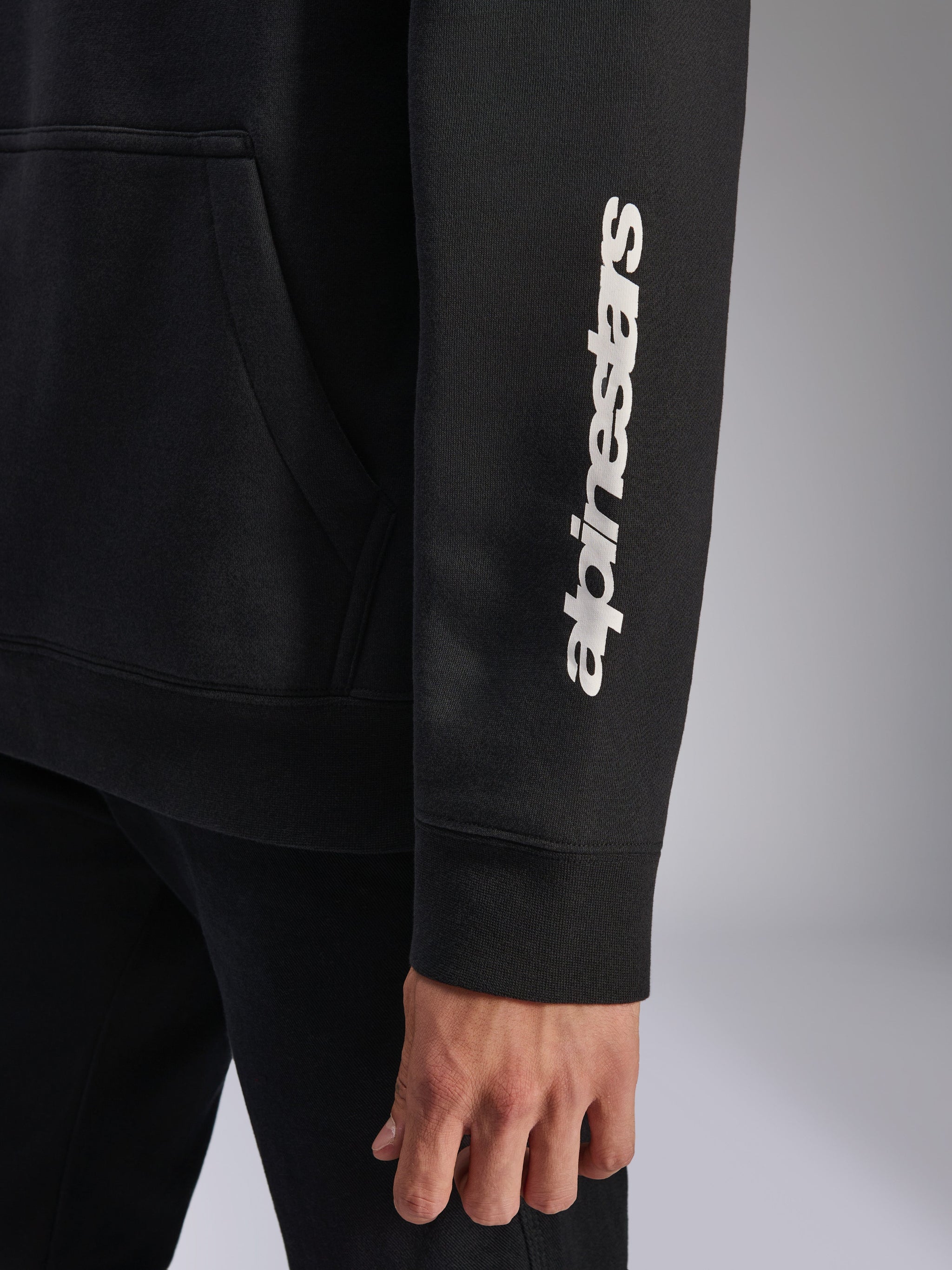 Alpinestars Harken hættetrøje, sort, nærbillede af ærme med lodret hvidt ordmærke-logo, ribmanchet og kængurulomme-detalje, afslappet sportswear fleece