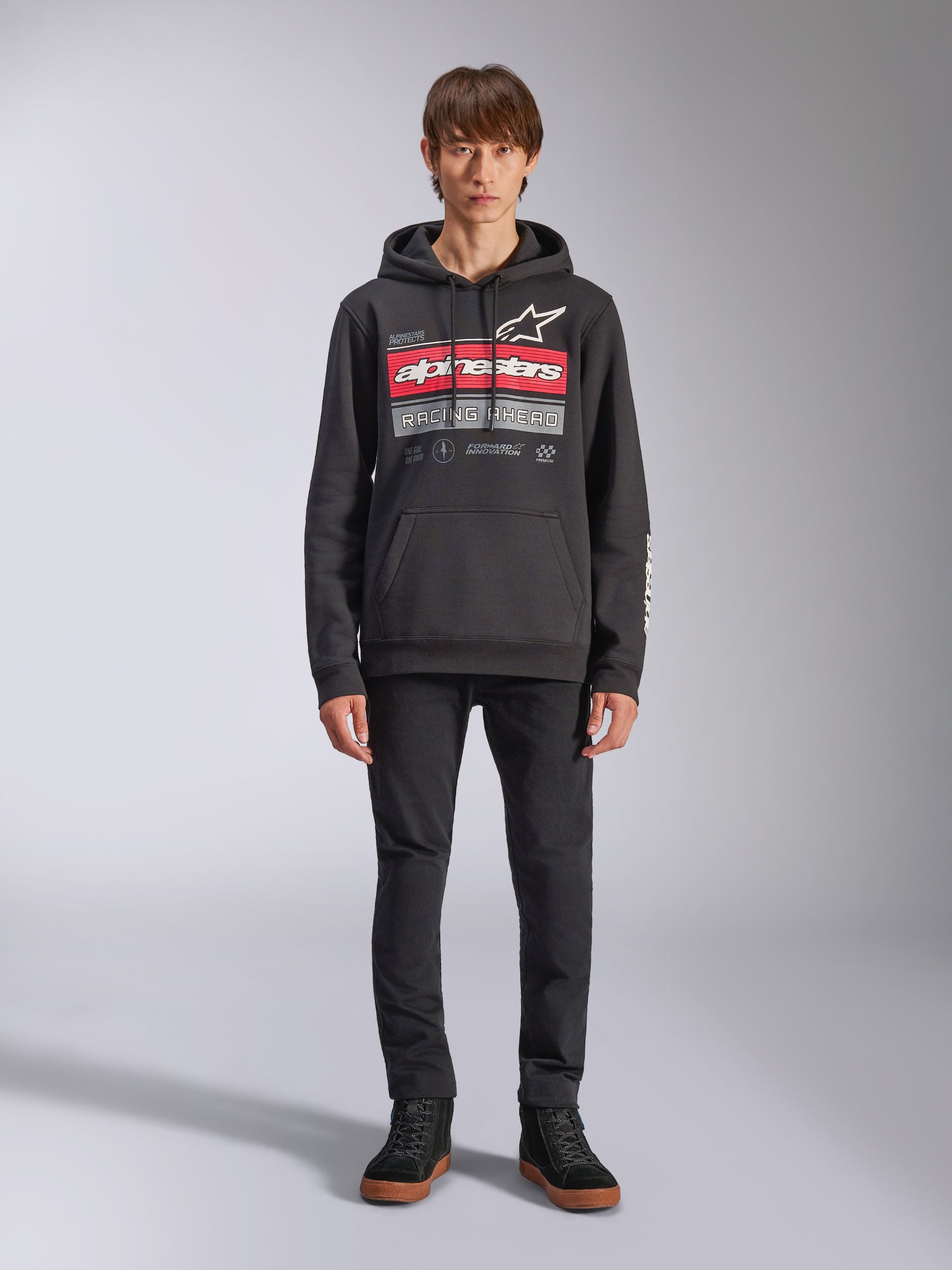 Alpinestars Harken hættetrøje, sort pullover-hættetrøje, iøjnefaldende brystgrafik med røde striber og 'Racing Ahead'-tekst, hvidt Astars-logo, kængurulomme, hætte med snoretræk, afslappet motorsport-inspireret streetwear