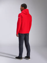 Alpinestars Frontal hættetrøje, rød pullover fleece-hættetrøje, set bagfra med hvidt ordmærke-logo på ærmet, båret med mørke denimbukser og sorte sko, afslappet motorsport streetwear