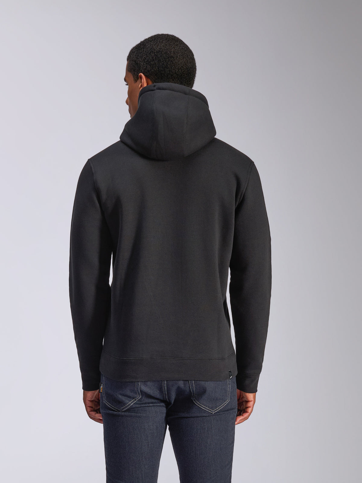 Alpinestars Blaze V3 Hættetrøje, sort pullover fleece-hættetrøje set bagfra, casual streetwear, med ribmanchetter og kant, jersey-foret hætte, båret med mørkeblå jeans