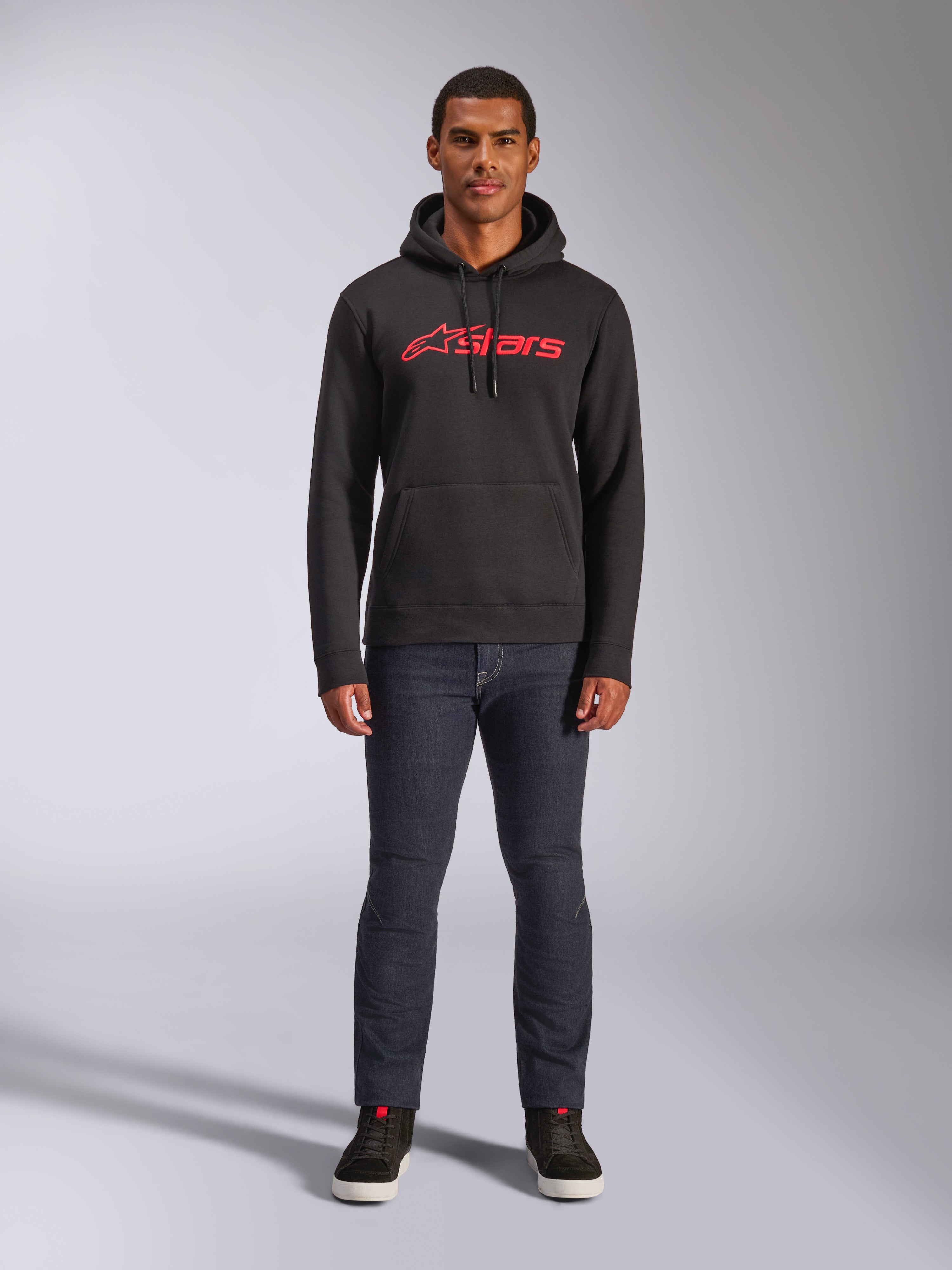 Alpinestars Blaze V3 hættetrøje, casual streetwear, sort med rødt Astars-logo, set forfra, båret af model med mørke denimbukser og sorte sneakers, moderne motorsport-inspireret fleecedesign