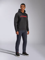 Alpinestars Blaze V3 hættetrøje, sort pullover-fleece med rødt Alpinestars-logo på brystet, båret af mandlig model med mørke denim-jeans og sorte sneakers, afslappet motorsport-inspireret streetwear