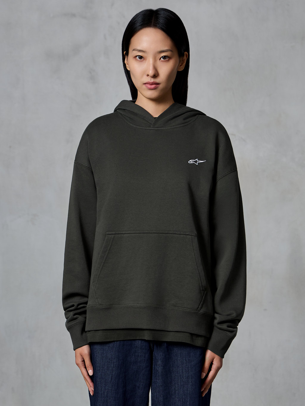 Alpinestars Essentials Ageless Hættetrøje, Off Black, båret af en model, med et lille hvidt Astars-logo på brystet, kængurulomme foran, stenvasket finish, afslappet premium fleece streetwear