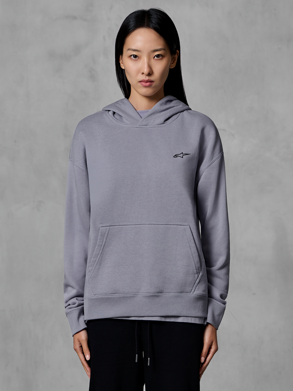 Alpinestars Essentials Ageless Hoodie, afslappet sportstøj, sølvfarvet med lille sort logo, kængurulomme, hættetrøje, båret af model, moderne livsstilsbeklædning