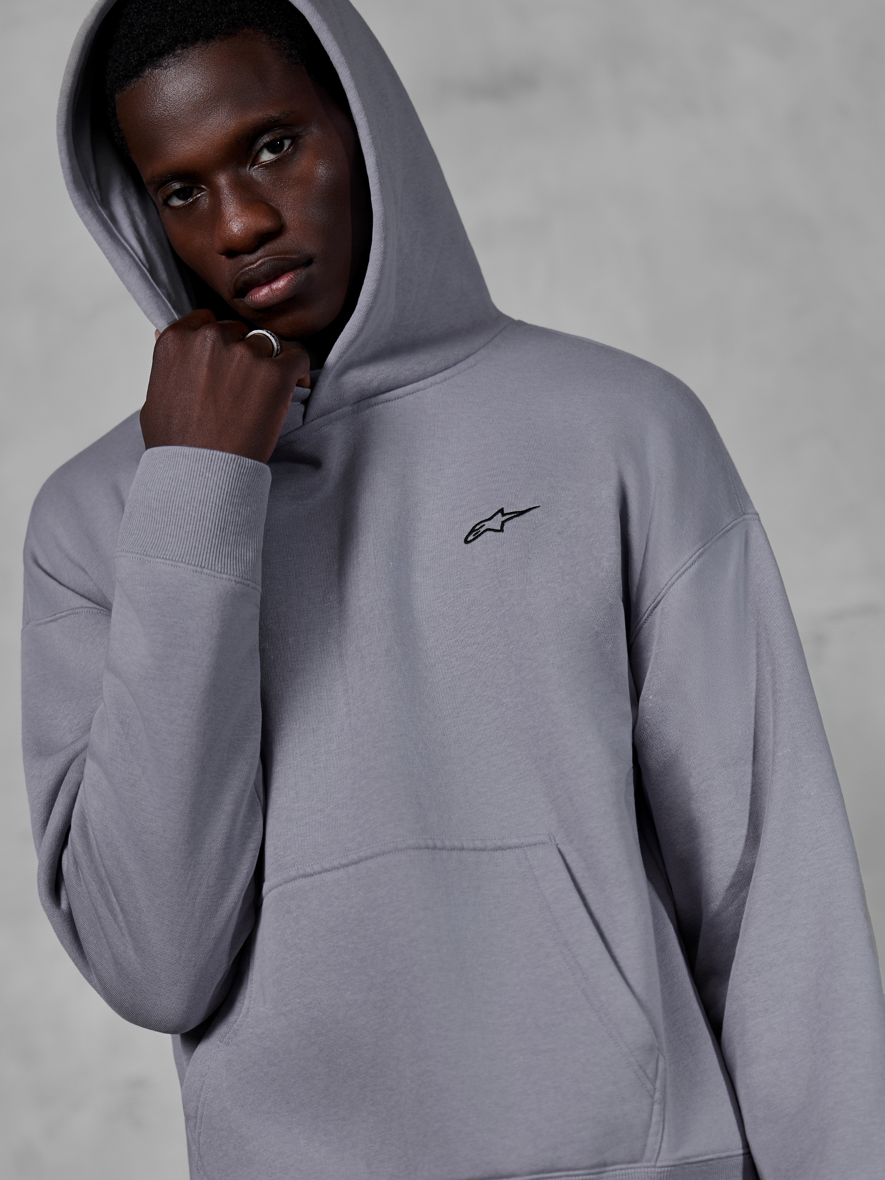 Alpinestars Essentials Ageless-hættetrøje, Silver, mandlig model iført hættetrøjen med hætten oppe, lille sort Alpinestars-logo på brystet, kængurulomme, ribbede manchetter, afslappet lifestyle-streetwear