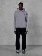 Alpinestars Essentials Ageless Hoodie, Silver, mandlig model i afslappet streetwear, lille sort Alpinestars-logo på brystet, kængurulomme foran, minimalistisk design, kombineret med sorte bukser og sneakers.