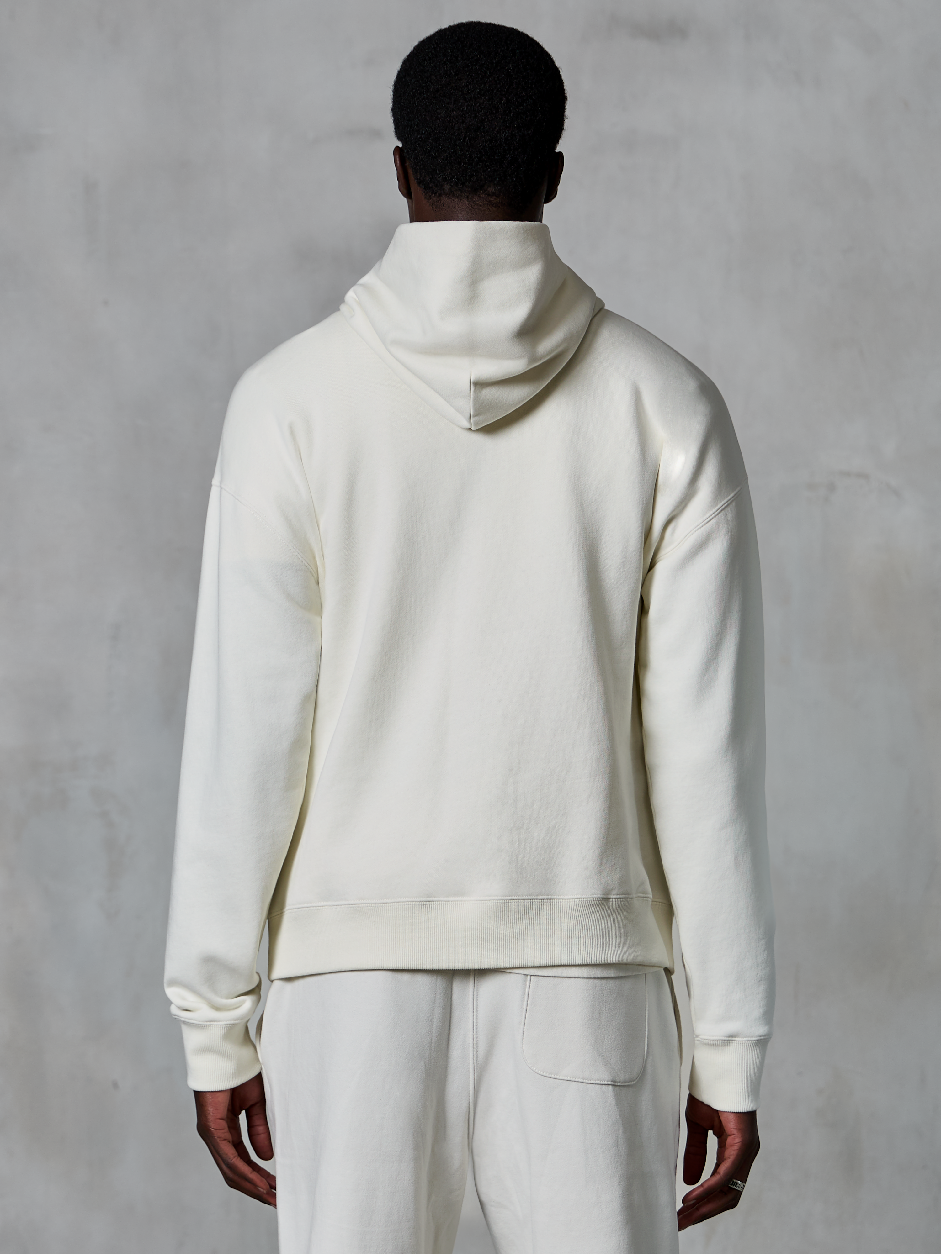 Alpinestars Essentials Ageless Hoodie, off-white pullover hættetrøje, set bagfra på model, rent minimalistisk design, matchende afslappede bukser, afslappet pasform til hverdagskomfort