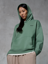Alpinestars Essentials Ageless Hoodie, casual streetwear, Cactus green with small black logo, hoodie worn with hood up, front kangaroo pocket, stone-washed finish, paired with light tan pants